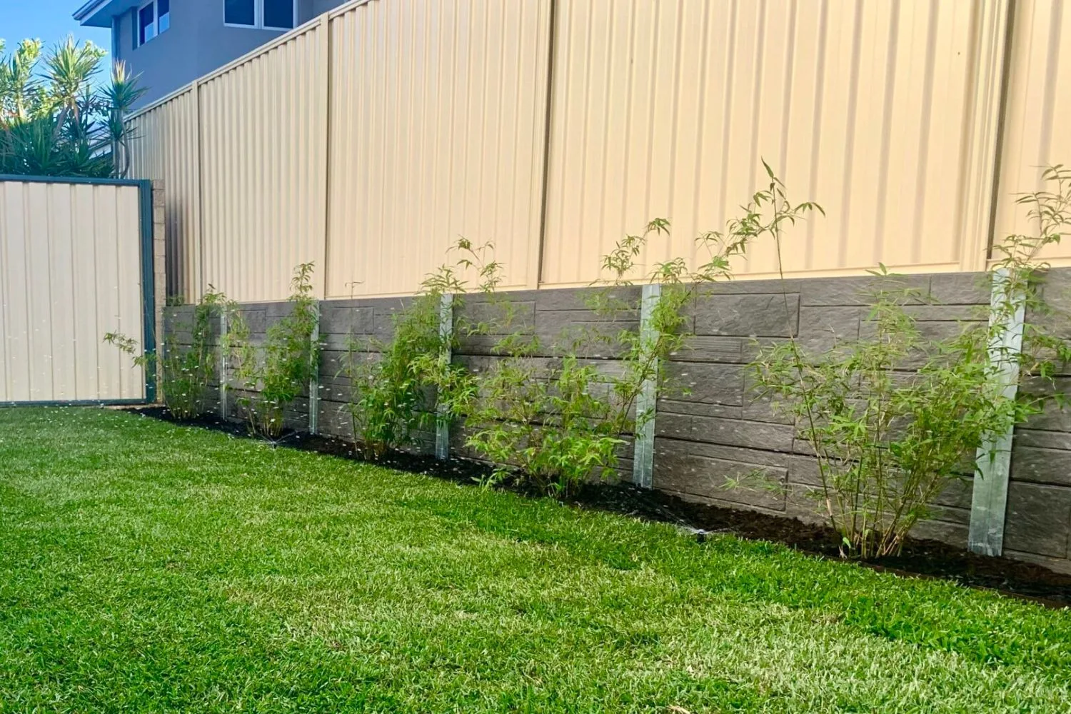 Rock-face concrete sleeper retaining wall below a Colorbond fence