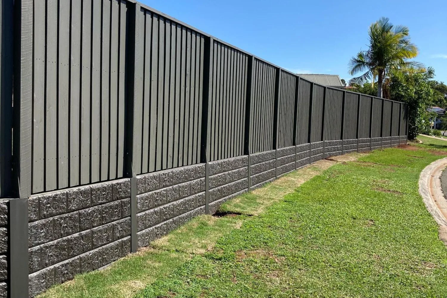 Long rock-face concrete sleeper retaining wall along a boundary fence