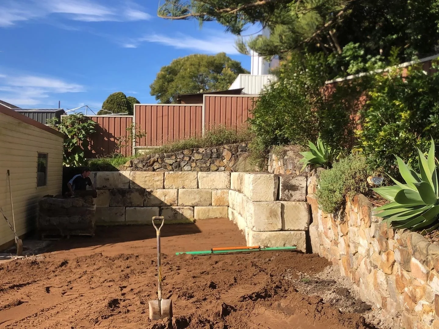 Sandstone block retaining wall under construction in a backyard