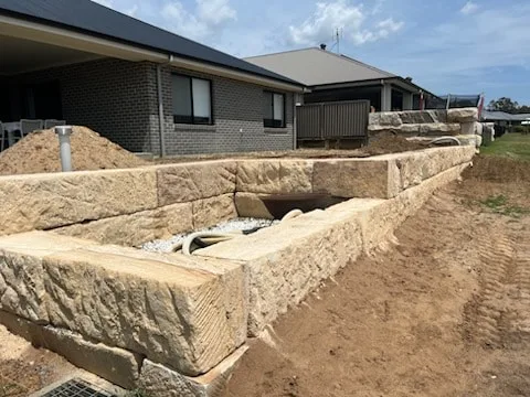 Large sandstone block retaining wall being built beside a new house