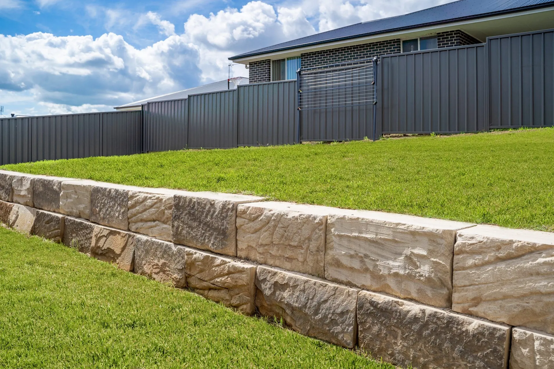 Sandstone block retaining wall along a lawn and Colorbond fence